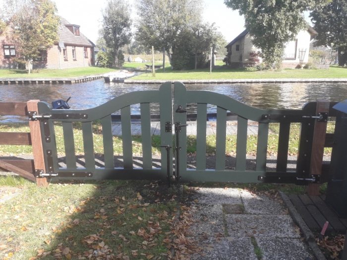 Donkergroene houten tuinpoort met uitzicht op een kanaal.